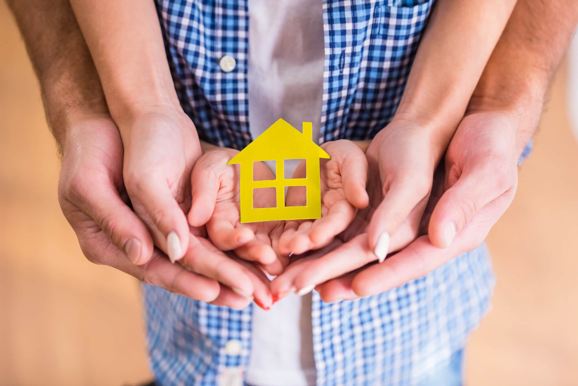 Die Hände von vier Personen halten einen gelben Papierausschnitt in Form eines Hauses, der das Zuhause und die Einheit der Familie symbolisiert.